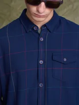 Camisa de manga larga en color azul noche con un patrón de cuadros finos en tonos rojos y verdes. Presenta cuello clásico, cierre frontal con botones y un bolsillo en el pecho con solapa.
