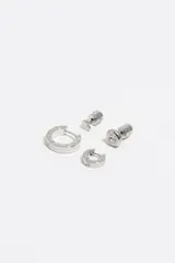 Set de cuatro pendientes de metal plateado que incluye un pendiente en forma de corazón, un pendiente circular con cristal central, una argolla mediana y una argolla pequeña, ambas con detalle de letras grabadas.