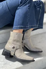Botas cortas color visón de cuero charolado, con punta cuadrada, caña media y detalle de arnés con hebillas plateadas. Taco cuadrado de altura media color negro.