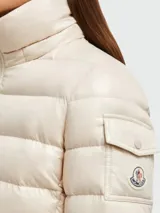 Campera puffer color crema de Moncler, modelo Badyf, con relleno de plumas, cierre frontal con cremallera, bolsillos laterales con cremallera y capucha con borde de piel sintética.