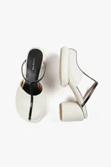 Mules de cuero color blanco con diseño moderno, taco ancho y plataforma. Cuenta con una tira superior negra que aporta estabilidad y un calce cómodo.
