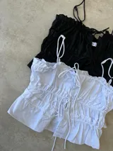 Top negro con breteles finos, escote recto con volantes y lazo ajustable en el centro.