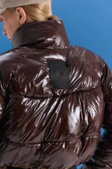 Campera puffer corta de acabado brillante en color marrón oscuro, con cuello alto, cierre frontal y diseño acolchado.