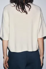 Jersey de punto color crema, confeccionado en 100% lana, con cuello redondo y mangas cortas anchas, de calce amplio.