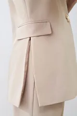 Chaleco largo de corte sastrero en color beige, con escote en V profundo, cierre frontal con un botón metálico y bolsillos laterales con solapa.