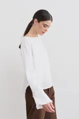 Blusa de lino con cuello bote y mangas largas terminadas en puños acampanados con volados. Presenta un cierre con botón en la espalda.