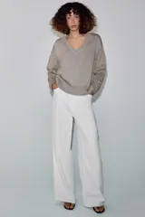 Sweater de punto grueso color beige, con cuello en V profundo y mangas largas. Cuenta con terminaciones acanaladas en el cuello, los puños y el ruedo.