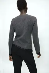 Top de manga larga en tejido de punto suave color gris, con cuello redondo y bajo asimétrico decorado con encaje negro a tono. Presenta detalles de encaje negro en los puños.
