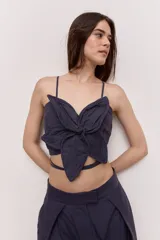 Blusa crop azul marino con tirantes finos y detalle de nudo frontal con forma de flor, con tiras para atar en la cintura.
