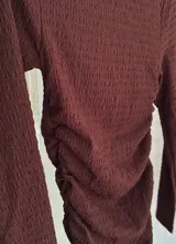 Vestido corto de manga larga en color bordó, con cuello alto y diseño ajustado con frunces laterales que recorren toda la prenda.