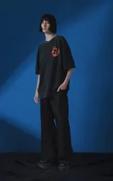 Remera de manga corta con cuello redondo y calce oversize, color negro con efecto nevado. Presenta una estampa frontal en color naranja con diseño gráfico de un rostro rodeado de llamas y texto tipográfico.
