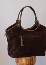 Cartera tipo tote de gamuza negra, con doble asa de mano y correa larga ajustable y desmontable. Cuenta con un diseño estructurado y base plana.