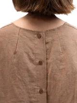 Remera de lino con corte holgado, cuello redondo y mangas cortas. Presenta un diseño minimalista con detalle de botones en la espalda.