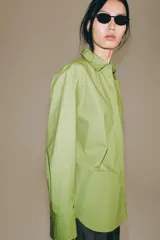Camisa oversize de popelín de algodón color verde claro, con cuello solapa y manga larga. Cierre frontal con botones ocultos y bajo redondeado.