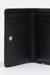 Billetera pequeña de estructura rígida, color negro, con estampado frontal en color dorado con la palabra "BIMBA". Posee cierre superior con tirador de tela amarillo mostaza.