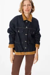 Chaqueta de denim azul oscuro con detalles en pana color tostado en el cuello, puños y ruedo. Presenta cierre frontal con botones metálicos y bolsillos frontales con solapa.