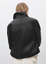 Chaqueta corta de efecto piel en color negro, con cuello de solapa, cierre frontal de botones y dos bolsillos de parche con solapa en la parte delantera. Presenta un diseño recto y forro interior.