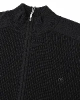 Campera de tejido de punto acanalado en color negro, con cuello alto y cierre frontal completo. Presenta un diseño minimalista con detalle de logo pequeño en el pecho.