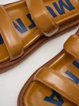 Sandalias de cuero vacuno color marrón con acabado brillante, diseño de dos tiras anchas acolchadas y plataforma baja.
