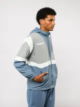 Campera de nylon Umbro con capucha, cierre frontal y diseño de bloques de color en gris, blanco y azul. Puños y dobladillo elásticos.