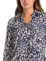 Camisa de manga larga con cuello camisero y cierre frontal de botones. Presenta un estampado abstracto en tonos azul marino y beige.