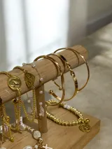 Set de cuatro pulseras esclavas rígidas en tono dorado. Incluye una pulsera con placa central plana, una pulsera fina lisa, una pulsera con nudo infinito y una pulsera con diseño retorcido.