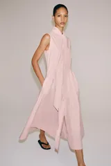 Vestido midi de Zara Woman Collection color rosado, confeccionado en hilatura de algodón. Presenta cuello subido con lazada, diseño sin mangas, bolsillos laterales ocultos y pliegues delanteros. Su falda tiene acabado en línea evasé y cuenta con cierre frontal mediante botones ocultos por solapa.