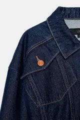 Chaqueta estilo bomber confeccionada en tejido denim azul oscuro. Presenta cuello solapa, cierre frontal con cremallera, mangas largas y bajo elástico. Incluye bolsillos delanteros de plastrón con solapa y botones.