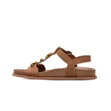 Sandalias planas de gamuza color marrón, con tiras anchas, hebilla metálica dorada de ajuste y detalles de apliques circulares dorados en el empeine.