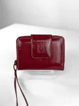 Mini billetera de cuero charolado color rojo, con cierre perimetral y solapa frontal con broche, decorada con un logo de búho grabado.