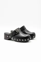 Zuecos negros de cuero vacuno con suela de madera, tachas metálicas y hebilla doble decorativa.