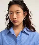 Camisa celeste con rayas verticales blancas, de corte alargado, cuello inglés y mangas largas.