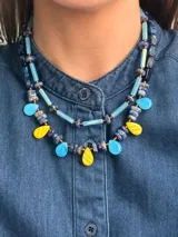 Collar corto con diseño multicolor compuesto por cuentas de cristal checo, piedras naturales y piezas de acrílico en tonos azul, celeste y amarillo, con cierre de cadena de acero quirúrgico.