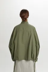 Campera bomber ligera color verde militar, confeccionada en 100% algodón, con bolsillos frontales con solapa, cierre de botones y cordón ajustable en el ruedo.