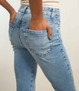 Pantalón bootcut de tiro alto en denim azul claro, ceñido en caderas y muslos con corte acampanado hacia el bajo y detalle de pequeña abertura lateral en los tobillos. Cuenta con bolsillos y cierre tradicional con botón y cremallera.