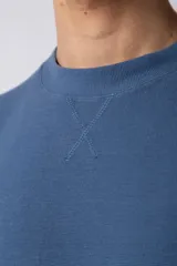 Remera de corte oversized en color marrón, confeccionada en tejido de algodón con textura de micropanal. Presenta cuello redondo con detalle de costura en forma de X y mangas cortas de estilo caído.