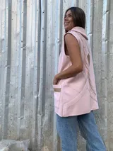 Chaleco de lana merino color rosado, con cuello alto tejido, cierre frontal tipo duffle con botones de madera y detalles en cuero sintético en los bolsillos y cierres.