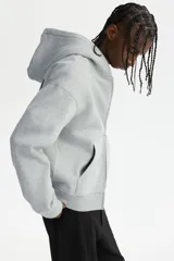 Campera con capucha de felpa gris, con cierre frontal completo, bolsillos tipo canguro y estampado tipográfico en el pecho. Presenta hombros caídos y puños acanalados.