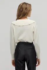 Sweater color crema de tejido de punto con lurex, escote en V con volados y mangas largas.