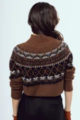 Sweater de punto color marrón, con cuello alto y diseño tejido con patrones geométricos en tonos negros y blancos en la parte superior y mangas.
