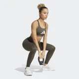 Top deportivo Adidas de soporte ligero, color verde oliva, con escote redondo y espalda tipo racer-back. Presenta el logo grande de Adidas en blanco en el pecho y en la pierna de un legging a juego.