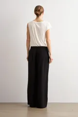 Pantalón de corte recto y tiro medio, confeccionado en tejido negro de textura sutil. Presenta un diseño minimalista con cierre frontal oculto y caída fluida.