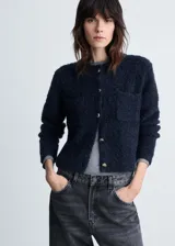 Chaqueta de punto bouclé en color azul marino, con cuello redondo, cierre frontal de botones efecto joya y dos bolsillos de parche delanteros.
