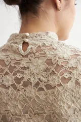 Media polera de encaje color beige, con cuello alto y mangas largas, de diseño translúcido y ajustado al cuerpo.