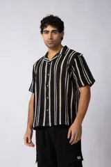 Camisa de manga corta tejida al crochet con diseño de rayas verticales en contraste de color negro y crudo, con cuello solapa y cierre frontal de botones.