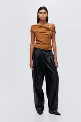 Top de punto fino color tostado con diseño asimétrico de un solo hombro. Presenta un panel fruncido en un brazo, manga corta con adorno metálico brillante y detalle drapeado en el lateral de la cintura.