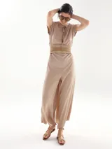 Mono largo color beige con cuello redondo, mangas cortas y cinturón trenzado a la cintura. Presenta aberturas laterales en las piernas y cierre con lazo en el cuello.