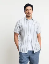 Camisa de manga corta con rayas verticales en tonos celeste, blanco, tostado y negro. Tiene cuello clásico, cierre con botones y bolsillo en el pecho.
