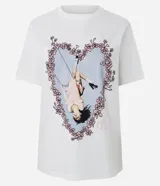 Remera blanca de algodón con cuello redondo y mangas cortas. En el frente presenta un estampado gráfico de Olivia Rodrigo colgada de una soga en un columpio, enmarcada por un diseño de corazón hecho con flores rosadas.