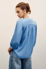 Camisa de poliéster color beige, con escote en V profundo, mangas 3/4 abullonadas y diseño fluido.
